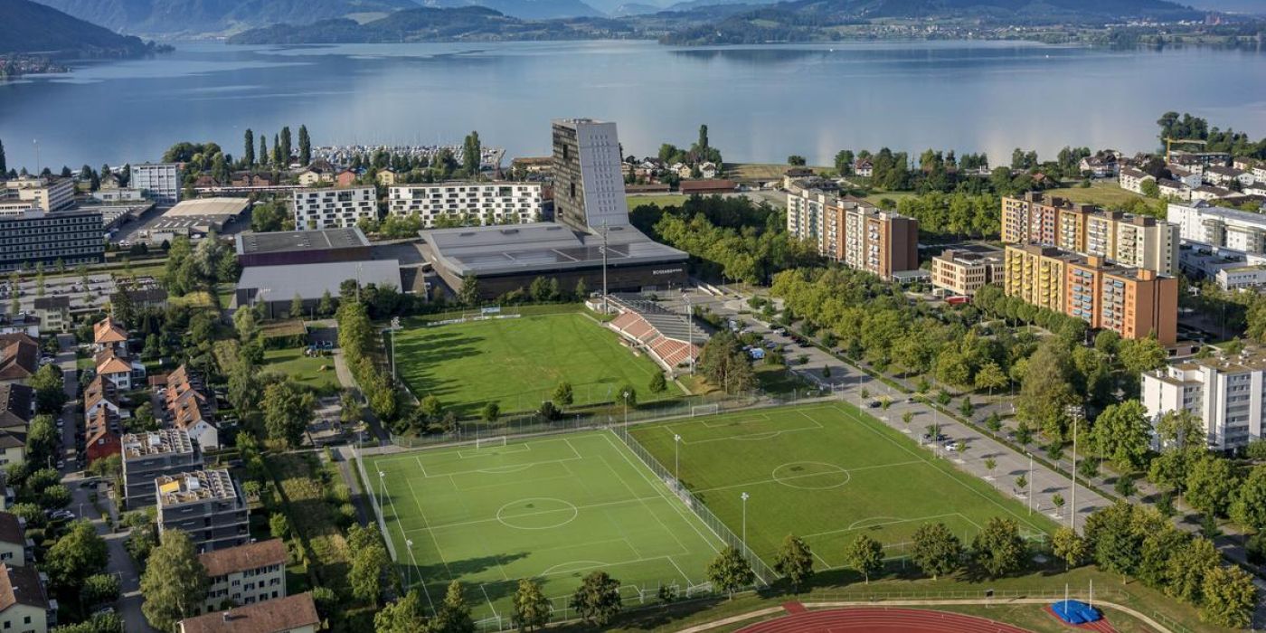 Bild zeigt die Schrägansicht des bestehenden Sportareals der Bossardarena mit dem Zugersee im Hintergrund.